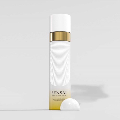 Eine weiße zylindrische Flasche mit Goldband, beschriftet 'SENSAI Absolute Silk Micro Mousse Treatment', steht auf flacher Oberfläche.