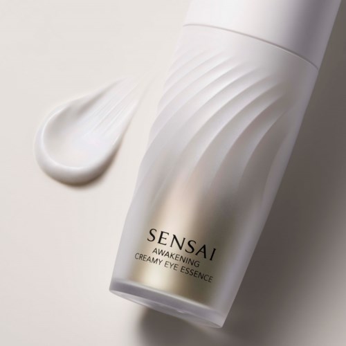 Eine weiße Flasche Sensai Awakening Creamy Eye Essence mit Creme daneben.