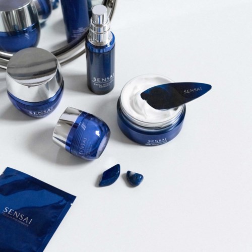 Blaue Hautpflegeprodukte mit silbernen Deckeln und ein weißer Creme-Stick werden gezeigt. Es gibt kleine blaue Probeschows und eine Packung.