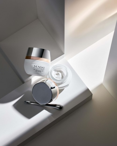 Hautpflegeprodukte, darunter Creme und ein Glas, stehen auf einem weißen Regal in der Nähe eines Fensters.