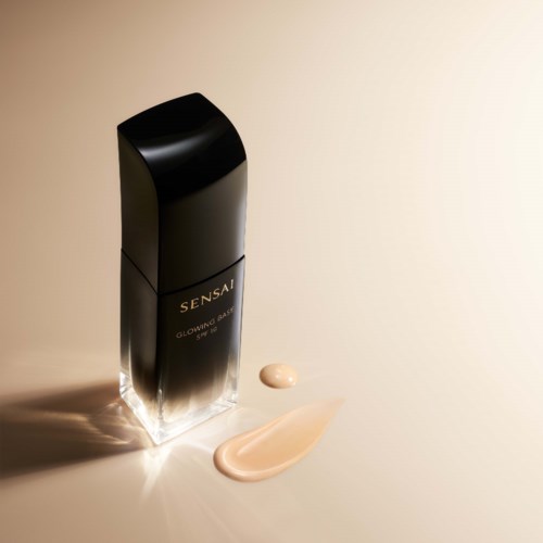 Black bottle of skincare with light pink cream and a small amount of cream under sunlight.
