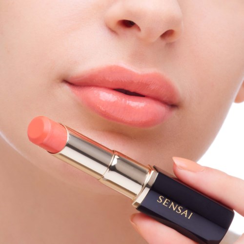 Nahaufnahme von den Lippen einer Person, die einen Lippenstift mit der Aufschrift 'SENSAT' hält.