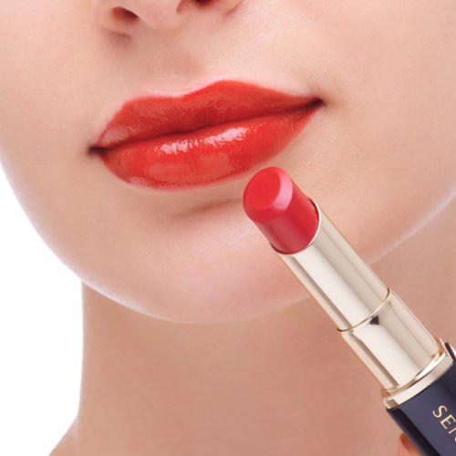 Eine Person trägt roten Lippenstift auf, die Lippen sind leicht geöffnet und glänzend.