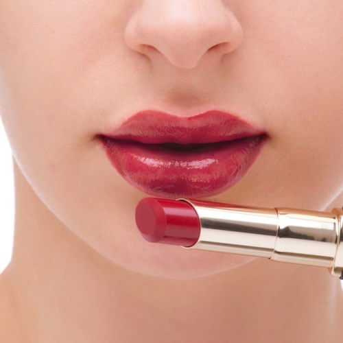 Eine Person trägt roten Lippenstift auf die Lippen auf, Nahaufnahme des Mundbereichs.