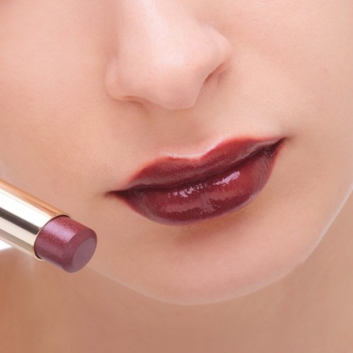 Nahaufnahme von Lippen mit dunklem, glänzendem Lippenstift und Lippenstifthersteller in der Nähe.