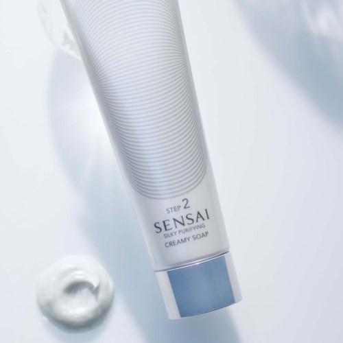 Eine weiße Tube Sensai silky purifying creamy soap mit blauer Kappe und einer Portion Schaum daneben.