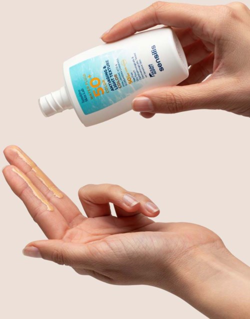 A person applies sunscreen lotion to their hand from a bottle labeled SPF 50.