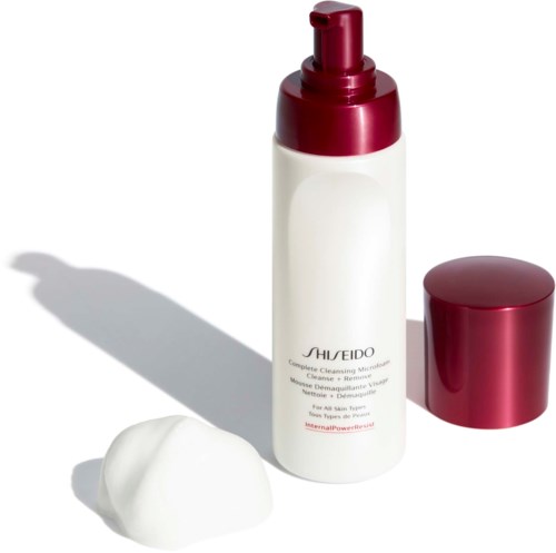 A white bottle with a red cap and pump, cream dollop beside it, and a red lid nearby. Skincare product setup.