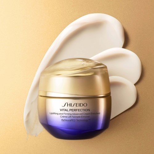 Ett guld- och lila krämglas från Shiseido Vital Perfection med vita klickar av kräm runt det.