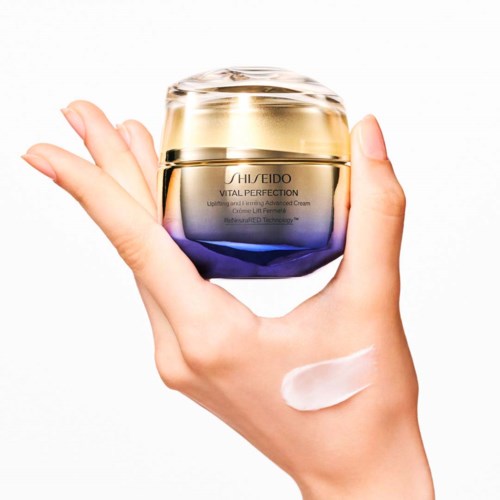 En hand håller i en burk med Shiseido hudvårdskräm, med lite grädde på handens baksida. Burken är glänsande och färgglad.