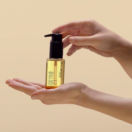 Eine Person hält eine kleine gelbe Flasche mit einem schwarzen Pumphahn, wahrscheinlich ein Hautpflege- oder Kosmetikprodukt.