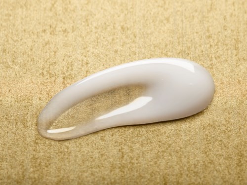 Een lepeltje witte crème of lotion op een beige oppervlak, in een gebogen vorm met een glanzende uitstraling.