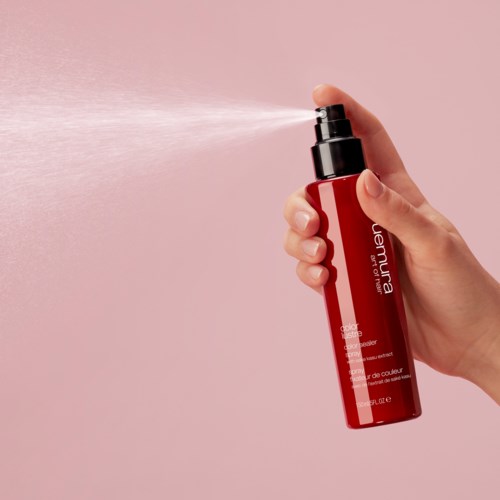 Een hand spuit een roze achtergrond met een roze fles met het label "keratine" of "kleurbehandeling."