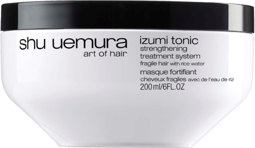 Ein weißer Behälter mit schwarzem Deckel, beschriftet 'Shu Uemura Izumi Tonic' zur Stärkung zerbrechlicher Haare mit Reiswasser.