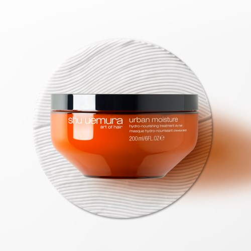 Ein Eimer Shu Uemura Urban Moisture feuchtigkeitsspendende Haarkur auf weißem strukturiertem Hintergrund.