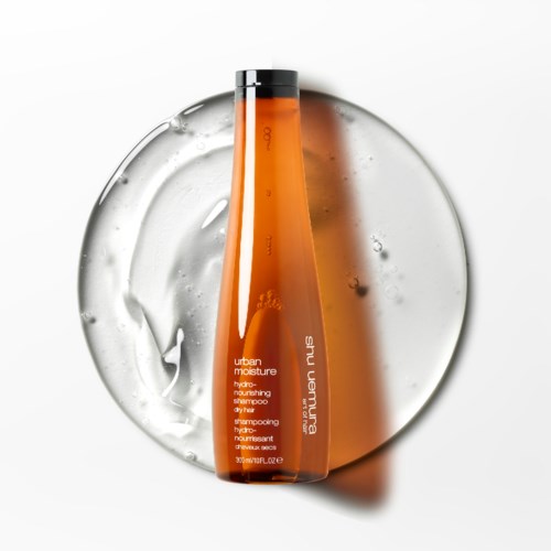 Eine orangefarbene Shampooflasche mit Beschriftung 'urban moisture' auf einer spiegelnden Oberfläche mit Wasser spritz.