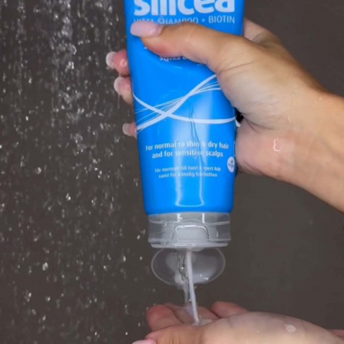 Hands pouring shampoo from a blue bottle onto the palm over a gray background.