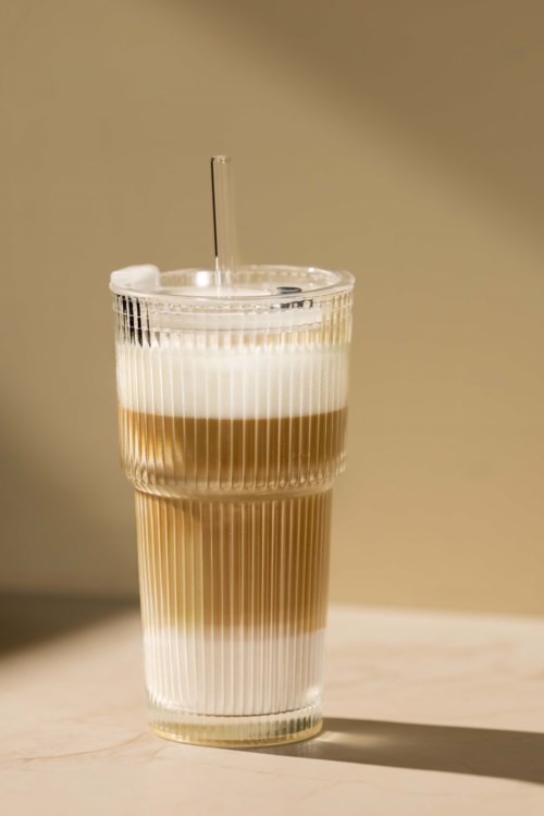 Ein gestufter Drink in einem klaren Glas mit Strohhalm, zeigt verschiedene Kaffee- oder Milchschichten, auf heller Oberfläche.