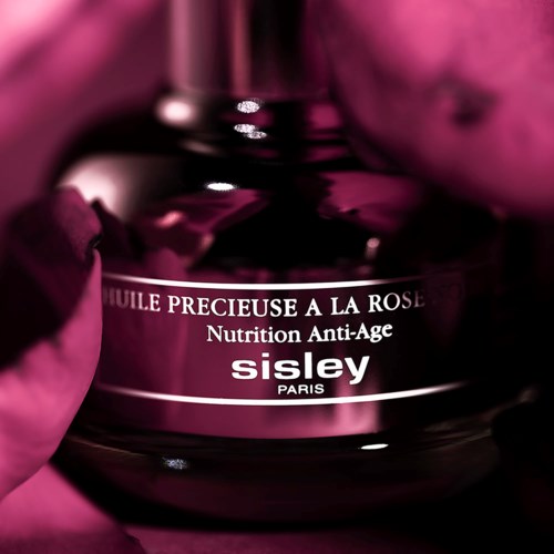 Een donkerroze fles met het label 'Sisley Paris' en de woorden 'Essential Rose Oil' en 'Anti-Age Nutrition'.