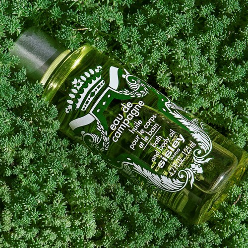 A green glass bottle with decorative white labels and text, lying among green plants or moss.