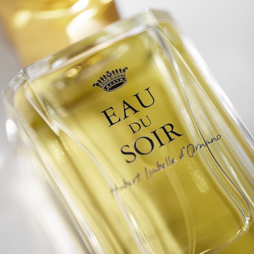 A glass bottle labeled 'Eau du Soir' with yellow liquid, a crown logo, and elegant text design.