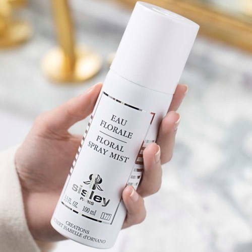 Dłoń trzyma białą butelkę spray z etykietą floral spray mist i kwiatowym wzorem.