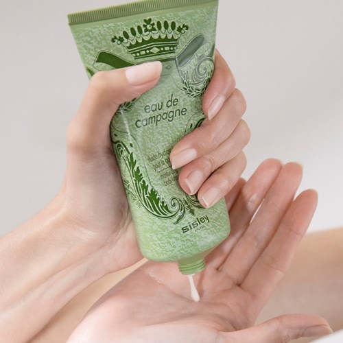 En hand trycker ut lotion från en grön tub till en annan hand, med neutral bakgrund.