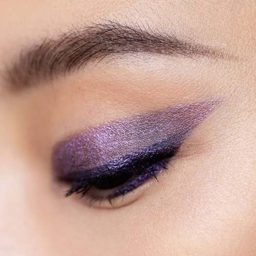 Close-up van het oog van een persoon met paarse en zwarte make-up en wenkbrauw.