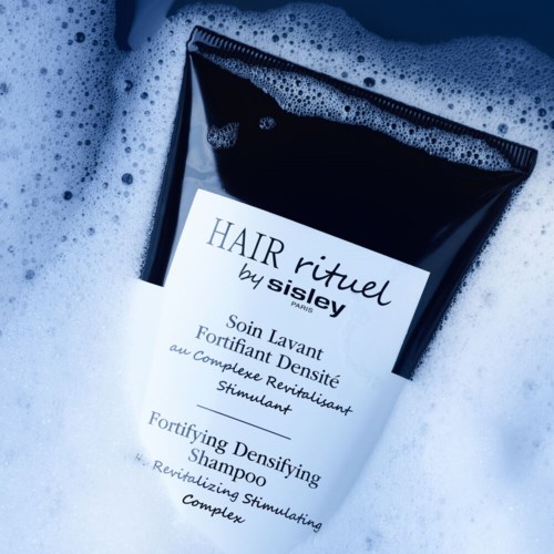 Een zwart-witte fles met 'Hair Ritual by Sisley' en schuim eromheen.