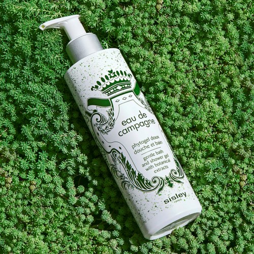 A white bottle with a pump lies on a bed of small green plants, labeled "eau de campagne" by Sisley.
