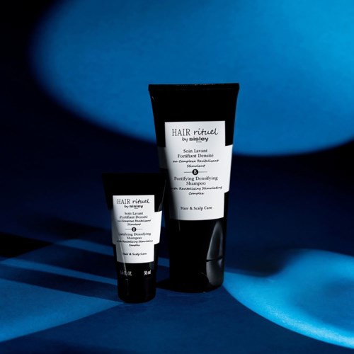 Two hair care products in black bottles with white labels, set against a blue background with light and shadow.
