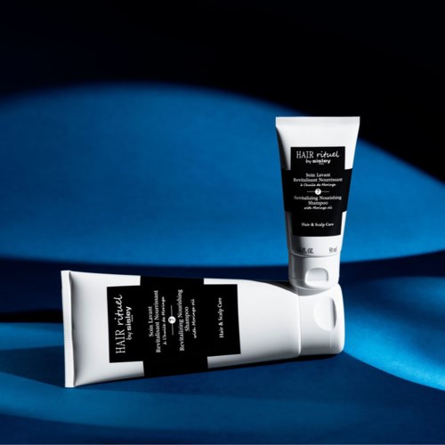 Twee haarverzorgingsproducten liggen op een blauwe ondergrond met een donkere achtergrond. Eén tube ligt, de andere staat.
