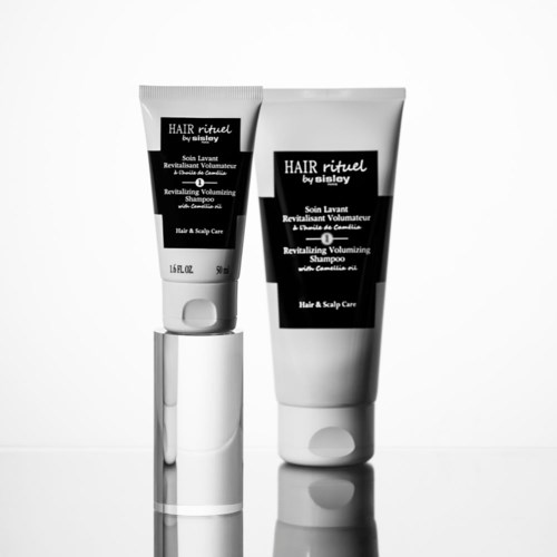 Two white and black hair care tubes, one larger than the other, with text on the labels, standing against a white background.