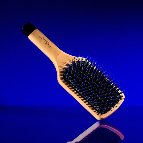 Een houten haarborstel met zwarte borstelharen en een zwarte grip, zwevend tegen een blauwe achtergrond.