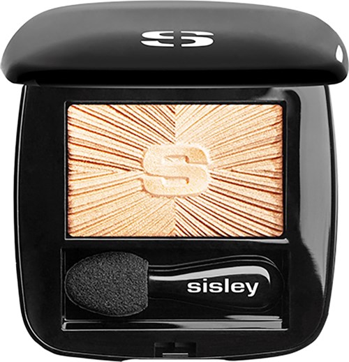 A black compact with a makeup brush, featuring a large letter 'S' on a radiant background.