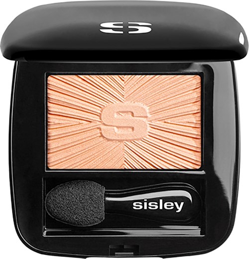 A compact with a peach-colored blush and a black applicator brush inside. The blush has a radiant sunburst design and a large 'S' in the center.