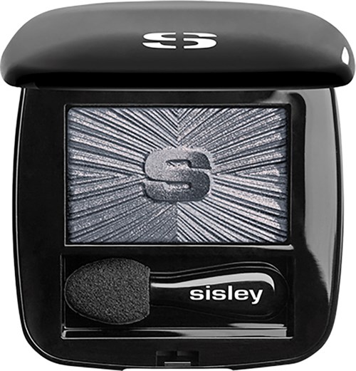 A black eyeshadow compact with a sponge applicator, featuring a logo and a sparkly, textured surface inside.