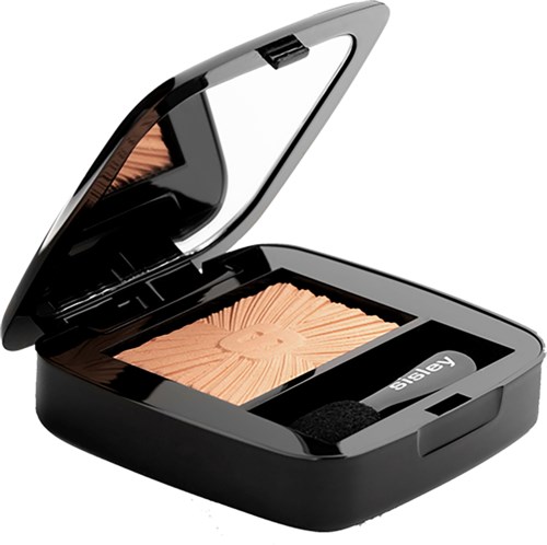 A makeup compact with a mirror open, containing peach-colored blush with a sun pattern and a black strap.