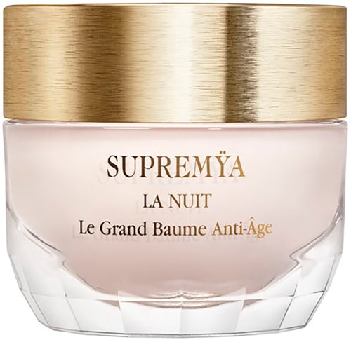 A jar of skincare cream with a gold lid labeled 'SUPREMYA La Nuit Le Grand Baume Anti-Âge' for night use.