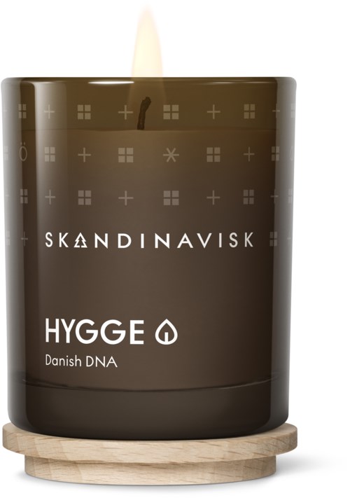 Eine dunkelbraune Kerze mit skandinavischem Design, beschriftet 'HYGGE Danish DNA,' auf einem Holztablett, mit kleiner Flamme.