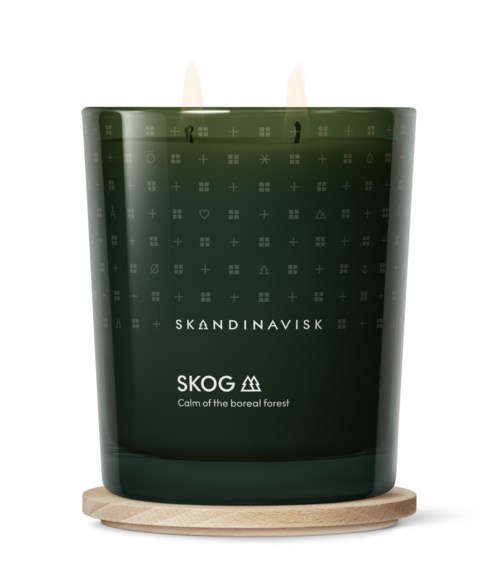 A green scented candle in a glass with Scandinavian branding, on a wooden base.