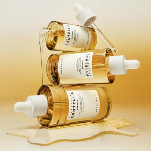 Three golden bottles with droppers, placed on a surface, with some liquid spilled around. Bright background.