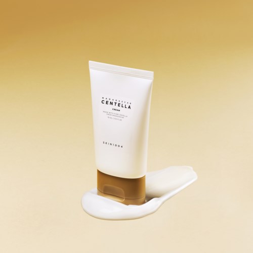 Eine weiße Tube mit der Aufschrift 'Centella', mit etwas Creme daneben auf beige Hintergrund.