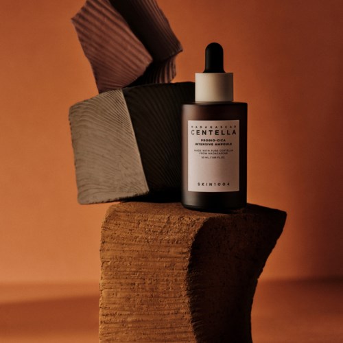 A skincare serum bottle with a dropper is placed on stacked textured blocks, against a warm background.