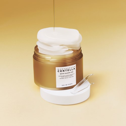 Een pot met witteksel, gevuld met witte crème, en een spatel voor een beige achtergrond.