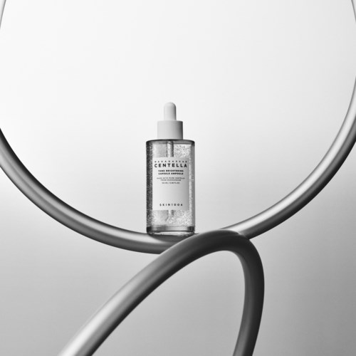 A small bottle with a dropper cap placed on a curved white surface, with a plain background.