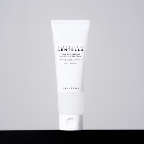 Ein weißer Tube mit der Aufschrift Madagascar Centella, mit schwarzen und grauen Texten, steht auf grauem Hintergrund.