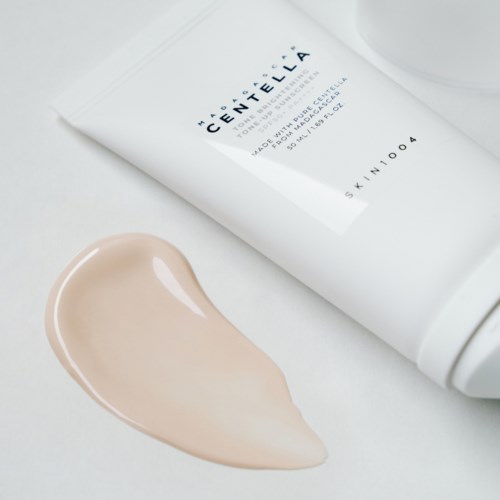 Eine Foundation-Tube mit beige Farbe, die auf einer weißen Oberfläche verschüttet wurde.