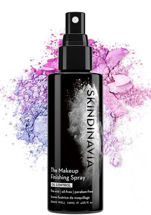 Eine schwarze Sprühflasche mit 'The Makeup Finishing Spray'-Aufdruck, hinter der violette und pinke Pulverstaub wirbeln.