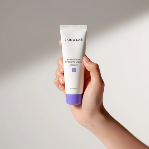 Een hand houdt een witte tube van Skin & Lab Barrierderm Intensive Cream met paarse dop, tegen een simpele achtergrond.